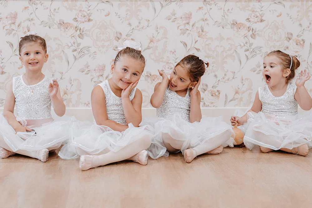 a group of 4 little girls wearing white tutus sitting in a dance studio