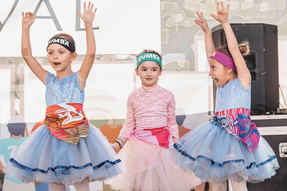 Three little girl dancing during a Zumba class, two of them wearing light blue tutu and one of them wearing a pink tutu